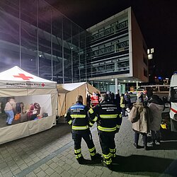 Zelt des BRK bei Ukraine-Hilfe-Einsatz mit Einsatzkräften und Menschen in der Nacht vor einem Gebäude