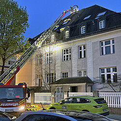 Brandbekämpfung beim Dachstuhlbrand: Gebäudeansicht mit Drehleiter 